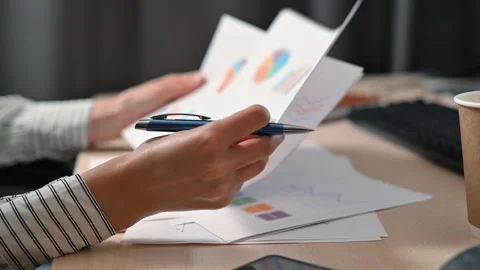 A person is working at a desk, reviewing documents with various charts and Stock Footage 339005859