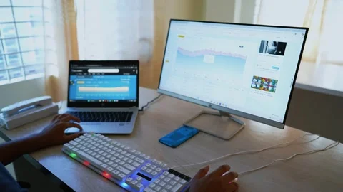 Person working on a desktop computer with a laptop beside it, analyzing dat.. Stockbeeldmateriaal 318056613