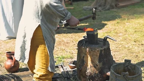 A person is working at a forge outdoors, using heat and tools to shape metal. Vídeo Stock 345036777
