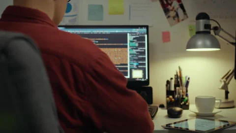Person working on programming tasks at a desk with computer and tablet late 動画素材 323871581