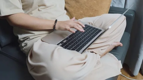 Person working remotely on laptop from comfortable sofa, typing on keyboard, Video stock 334461508