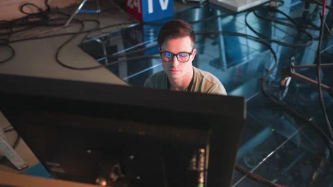 Person working in TV studio, wearing glasses, focused on computer monitor Stock Footage 317585260