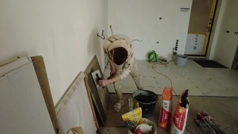 Person working on wall with tools in empty room during daylight hours in constru Stock Footage 332366757