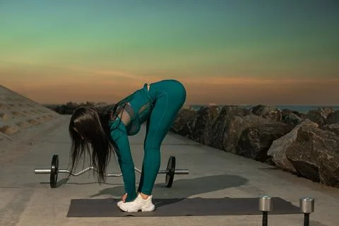 Person in workout attire is executing forward bend stretch on mat located along Stock Photos