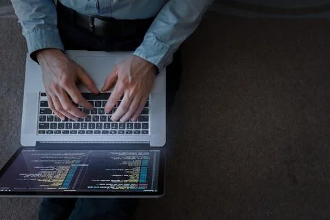 Person works on laptop with code on screen while sitting on the floor in a Fotos de archivo