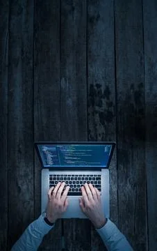 Person works on laptop with code on screen while sitting at wooden table in dim Foto stock