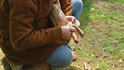 A person works on woodworking while sitting on the ground in a natural setting, 库存影片 345029078