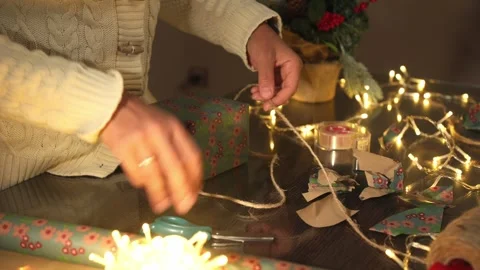 Person Wrapping Gifts with String and Festive Paper in Cozy Winter Setting Stock Footage 316962639