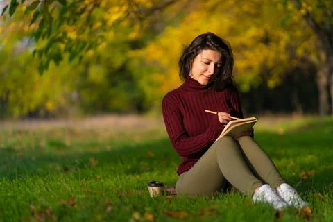 A person write notes sitting on a lawn in an autumn park. Joyful state of min Stock Photos
