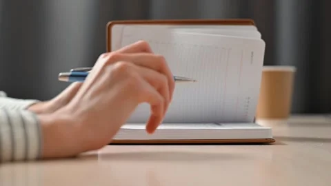 A person writes in a notebook using a pen while seated at a table. This moment Stock Footage 339005700