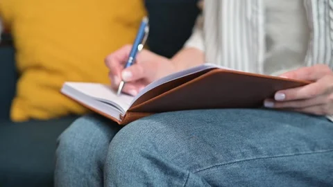 A person writes notes in a notebook while seated on a couch. The individual Stock-Footage 338446343