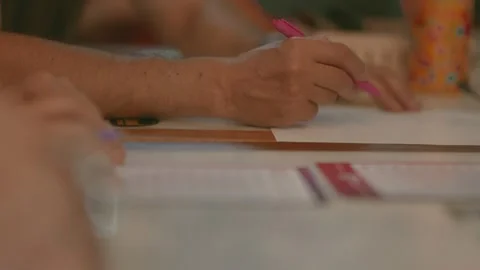 Person writes notes on paper with pink pen at cafe table during evening in city Stock Footage 335549388
