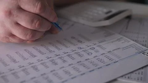 Person writes notes on paper while using a calculator at a desk to manage Stock Photos