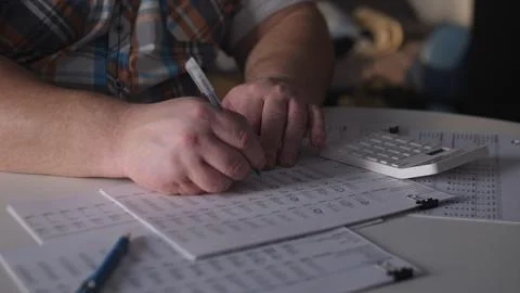 Person writes on sheets of paper while using a calculator on a table during an 스톡 사진