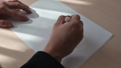 A person writes the word sun on a sheet of white paper using a yellow marker. Stock-Footage 337550068