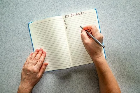 Person writing a to do list in a lined notebook with pen and hands on a table Stock Photos