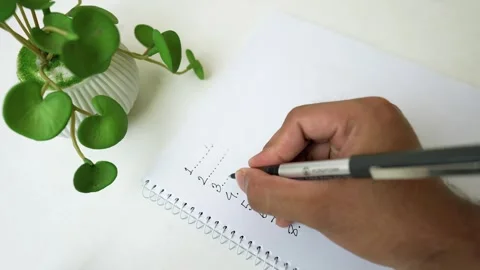 Person Writing Equations in Notebook Beside Plant Stock Footage 320726026
