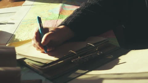 Person Writing Map Data into Clip Binder on Sunlit Desk 4K Stock Footage 332450033