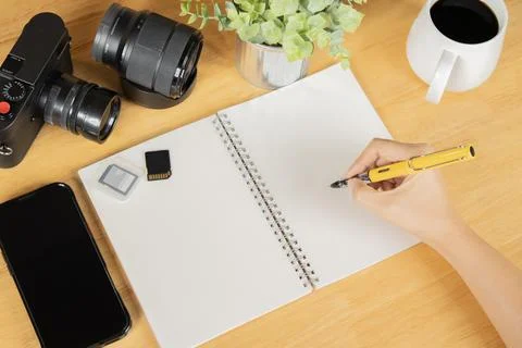 A person writing in a notebook with camera, memory cards, phone and lens on.. Stock Photos