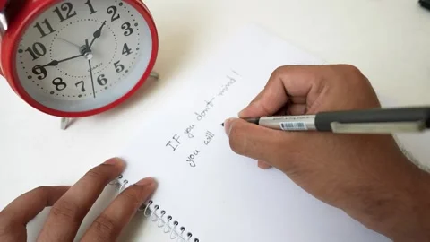 Person writing in a notebook with a red clock nearby Video stock 318578305
