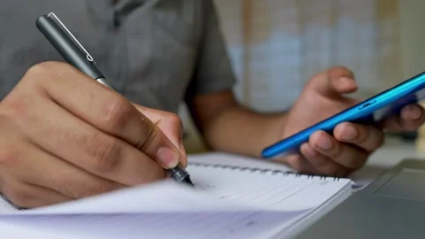 Person writing in a notebook while holding a smartphone, close-up Stock Footage 315982972
