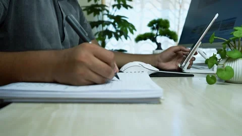 Person writing in a notebook while holding a smartphone, surrounded by plants Stock Footage 317737138