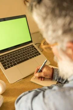 Person writing in notebook while looking at laptop screen Stock Photos