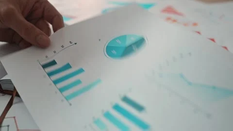 A person is writing in a notebook while reviewing colorful graphs and charts on Stock-Footage 338302481