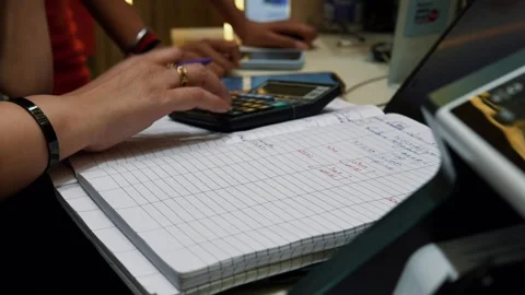 Person Writing in a Notebook While Using a Smartphone and Calculator at a Des Stock Footage 345363616