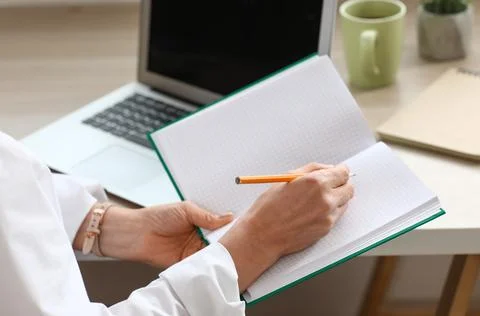 Person writing notes in grid notebook with pencil, laptop and coffee mug on d Stock Photos