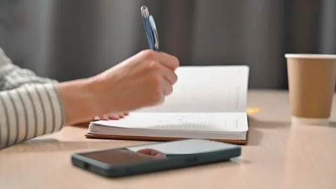 A person is writing notes in a notebook while holding a pen in their hand. A Stock Footage 339005771