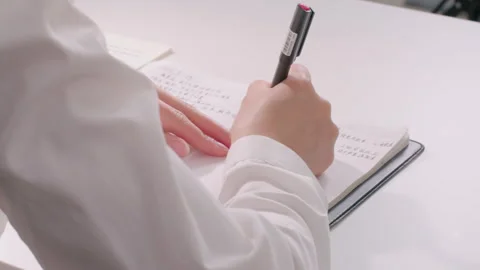 Person Writing Notes in Notebook on White Desk, Close-up Shot Vidéo 334847536