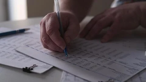Person writing notes while reviewing documents on a table during daytime in a Foto stock