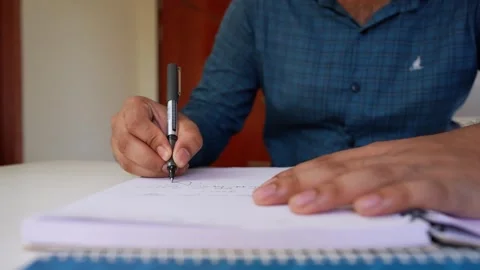 Person writing numbers in a notebook with a pen on a white surface Stock Footage 320724092