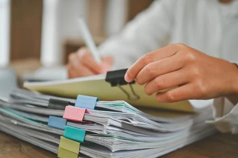 A person is writing on a stack of papers with a pen 스톡 사진
