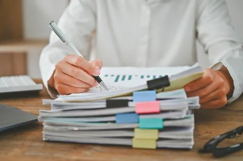 A person is writing on a stack of papers with a pen Stock Photos
