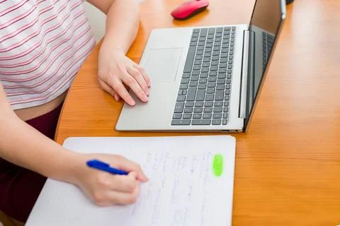 A person writting notes in a notebook with a blue pen while working on a laptop Stock Photos