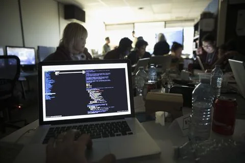 Personal perspective hacker coding on laptop at hackathon in dark office Stock-Fotos