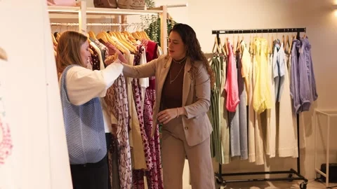 Personal stylist helping a client choose a dress in a boutique Stock Footage 337027366