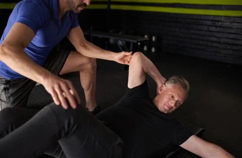 Personal trainer assisting elderly man with core ab crunch exercise Stock Photos