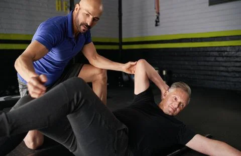 Personal trainer assisting elderly man with core ab crunch exercise Фото