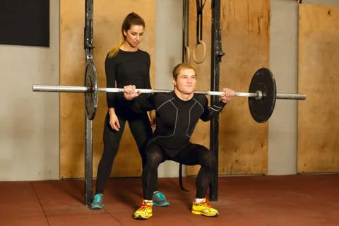 Personal trainer assisting in the squat exercise Stock Photos