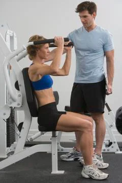 Personal trainer assisting woman on exercise machine Stock Photos