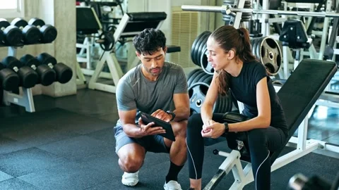 Personal trainer consulting a client by a weight bench in a gym, reviewing .. Stock Footage 347733579