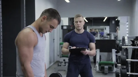 Personal trainer counts number of exercises man has with a barbell on bicep. Stock Footage 85129423