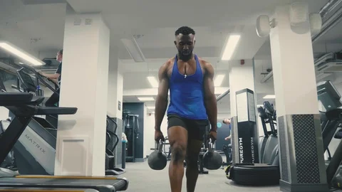 Personal trainer does kettlebell lunges across a gym floor Stock Footage 89577893