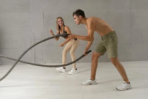 The personal trainer is engaged with the client on a battle rope in gym. Athl Foto stock
