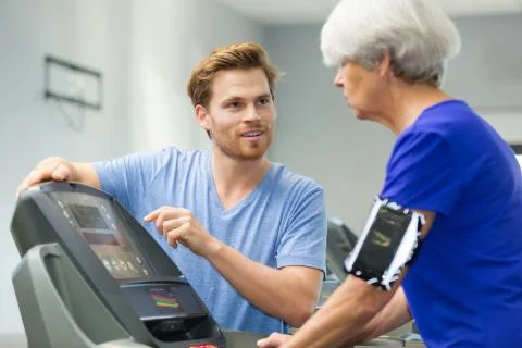 Personal trainer explaining treadmill controls to seniro woman Stock Photos