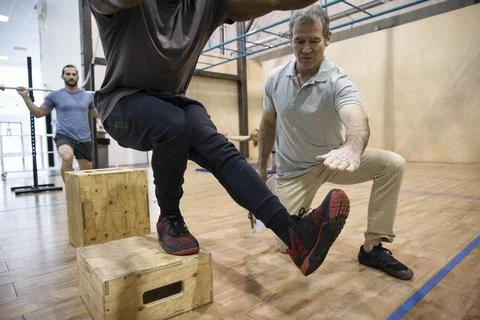 Personal trainer guiding client doing box exercise in gym Stock Photos