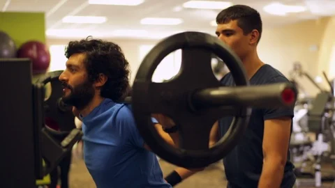 Personal trainer helping a client to lift weights on a weight machine at the 스톡 동영상 88404556